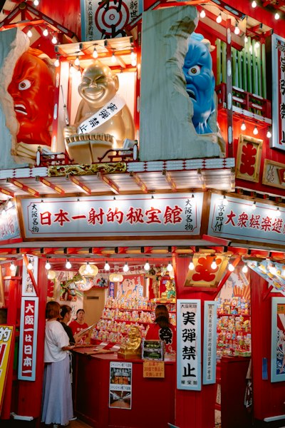 People At A Brightly Lit Red Stall With Colorful Statues In Osaka, Japan wallpaper preview