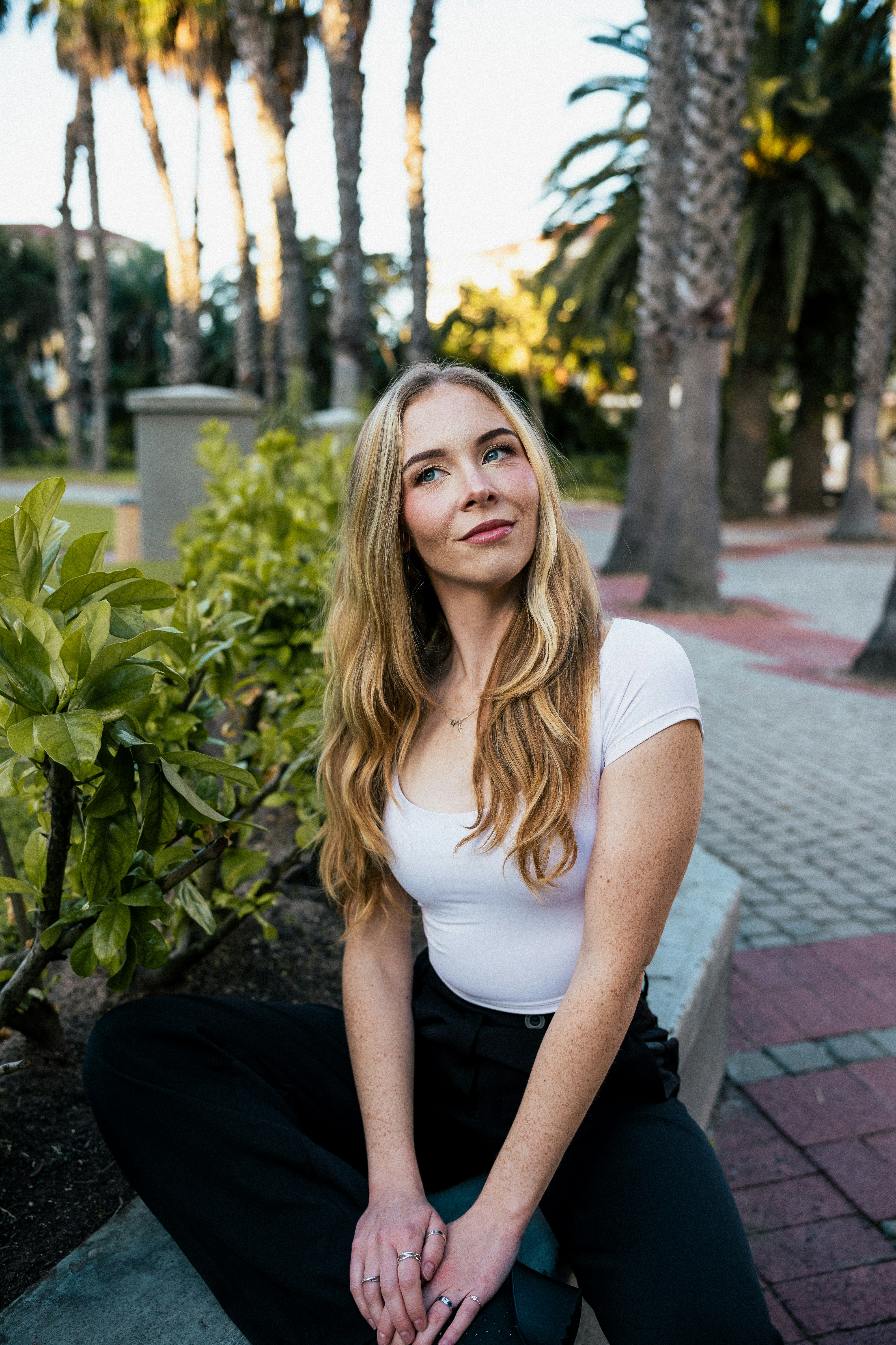 A Woman With Long Blonde Hair In A White Top Sitting On A Stone Wall HD mobile wallpaper