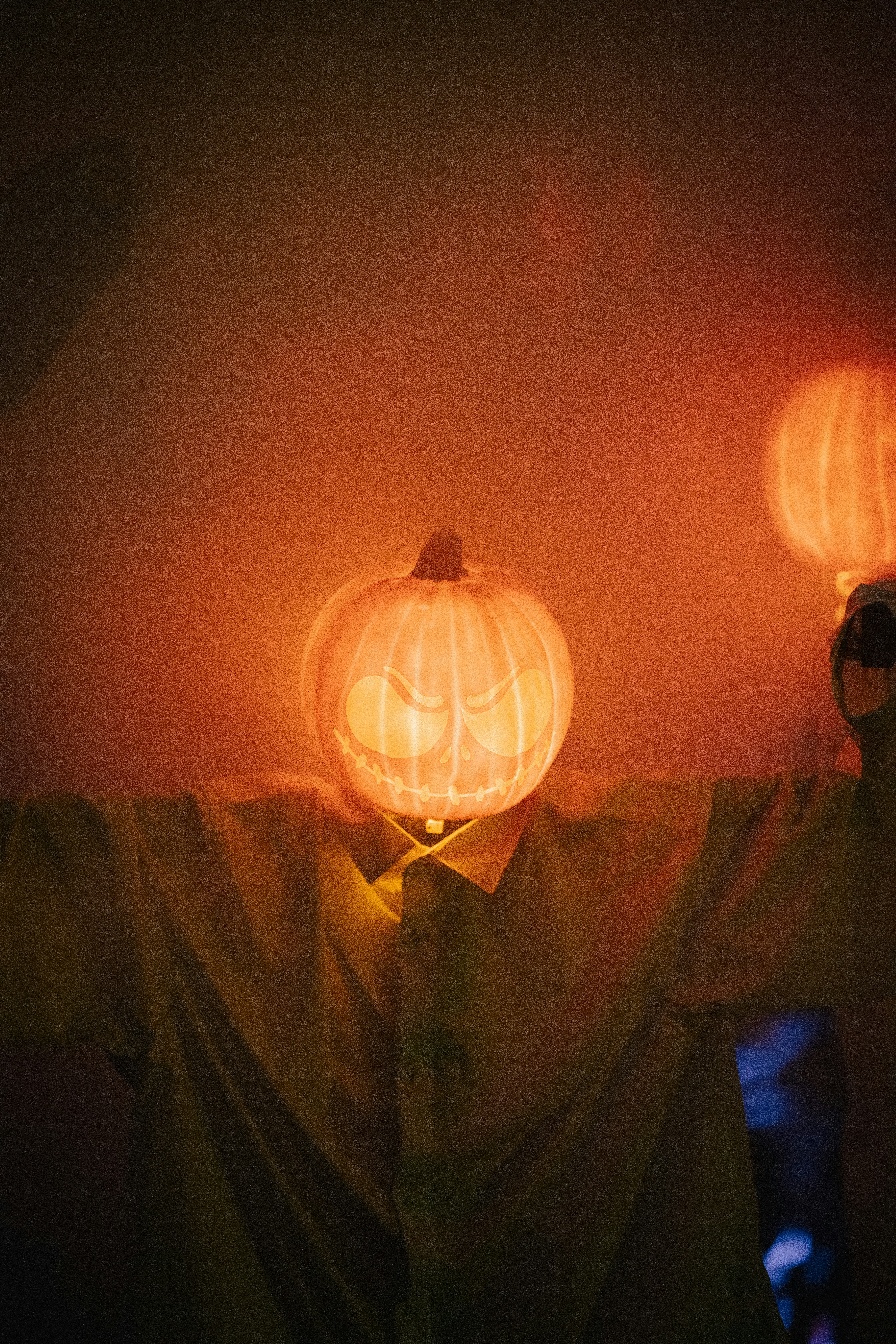 A Person Wearing A Glowing Jack-o'-lantern Mask With A Carved Face In A Dimly Lit Room HD mobile wallpaper