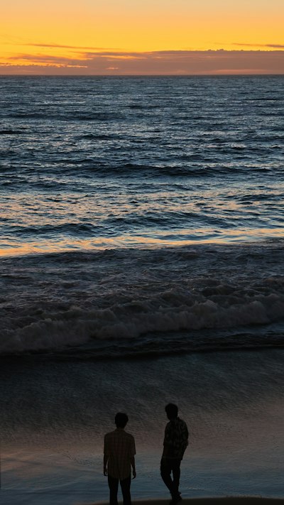 Two People In Silhouette On A Beach Under A Warm Orange Sky wallpaper preview