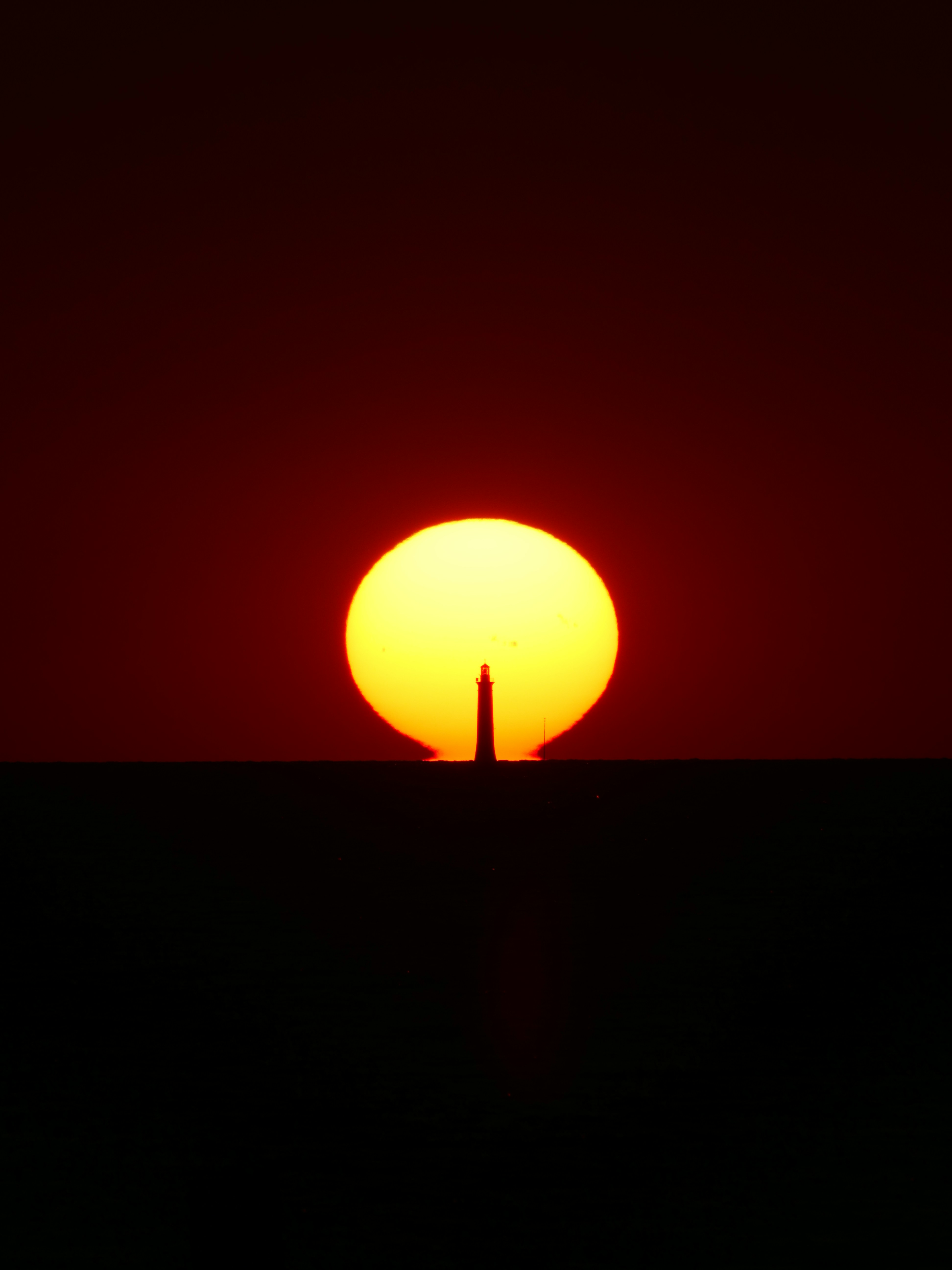 A Lighthouse Silhouette Centered Against A Large Low Sun On The Horizon HD mobile wallpaper