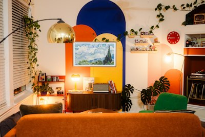 A Living Room With A Colorful Mural, A Television, And Indoor Plants wallpaper preview
