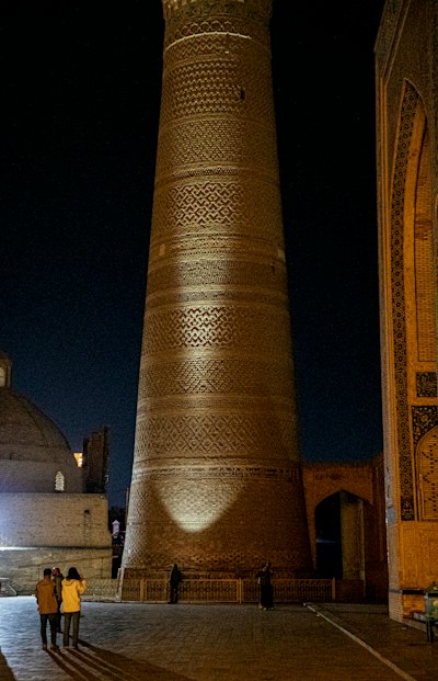 The Illuminated Kalyan Minaret At Night With People Walking In The Square In Bukhara wallpaper preview