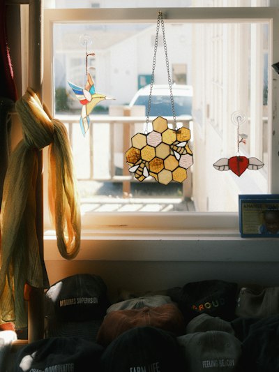 Stained Glass Ornaments Of A Hummingbird, Honeycomb, And Heart Hanging In A Sunlit Window wallpaper preview