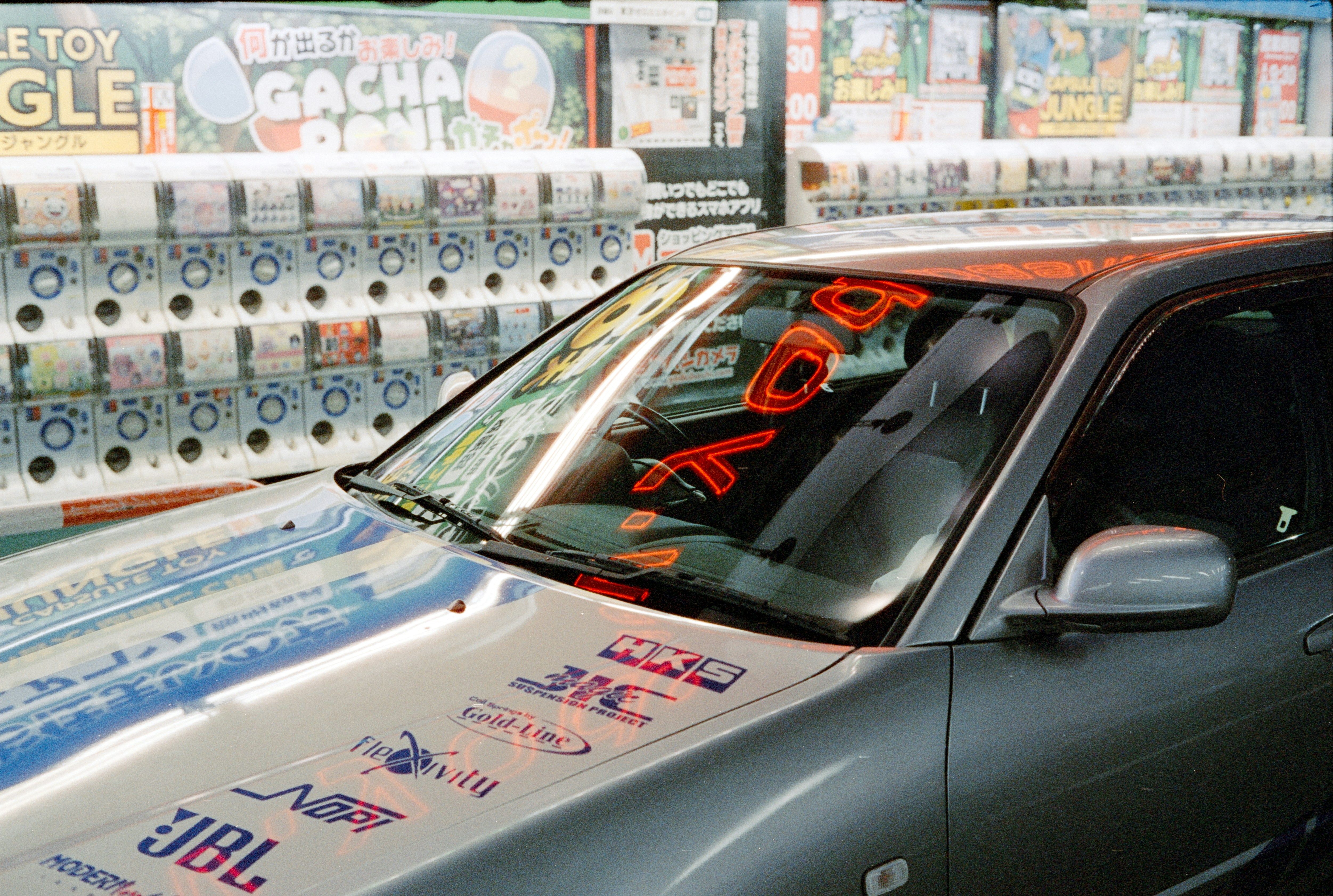 A Grey Car With Racing Decals Parked In Front Of A Row Of Capsule Toy Machines HD mobile wallpaper