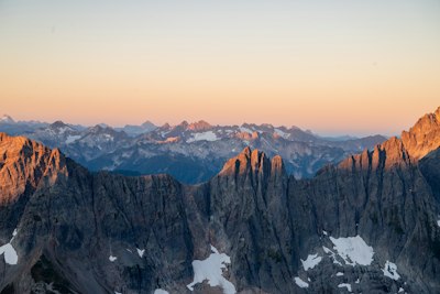 Jagged Mountain Peaks With Patches Of Snow Under A Soft Orange Sky wallpaper preview