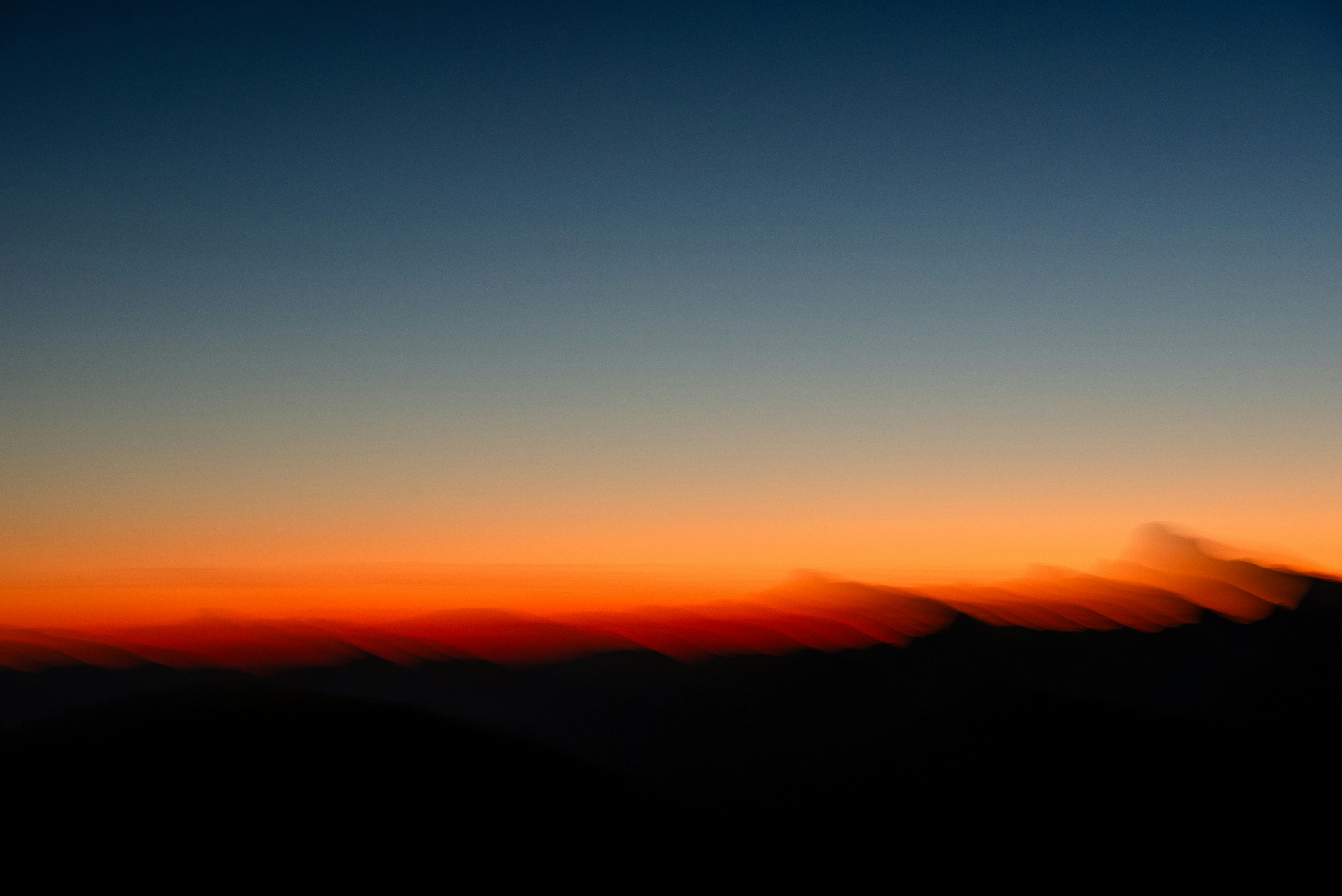 Blurred Mountain Silhouettes Against A Vibrant Orange And Deep Blue Sky HD mobile wallpaper