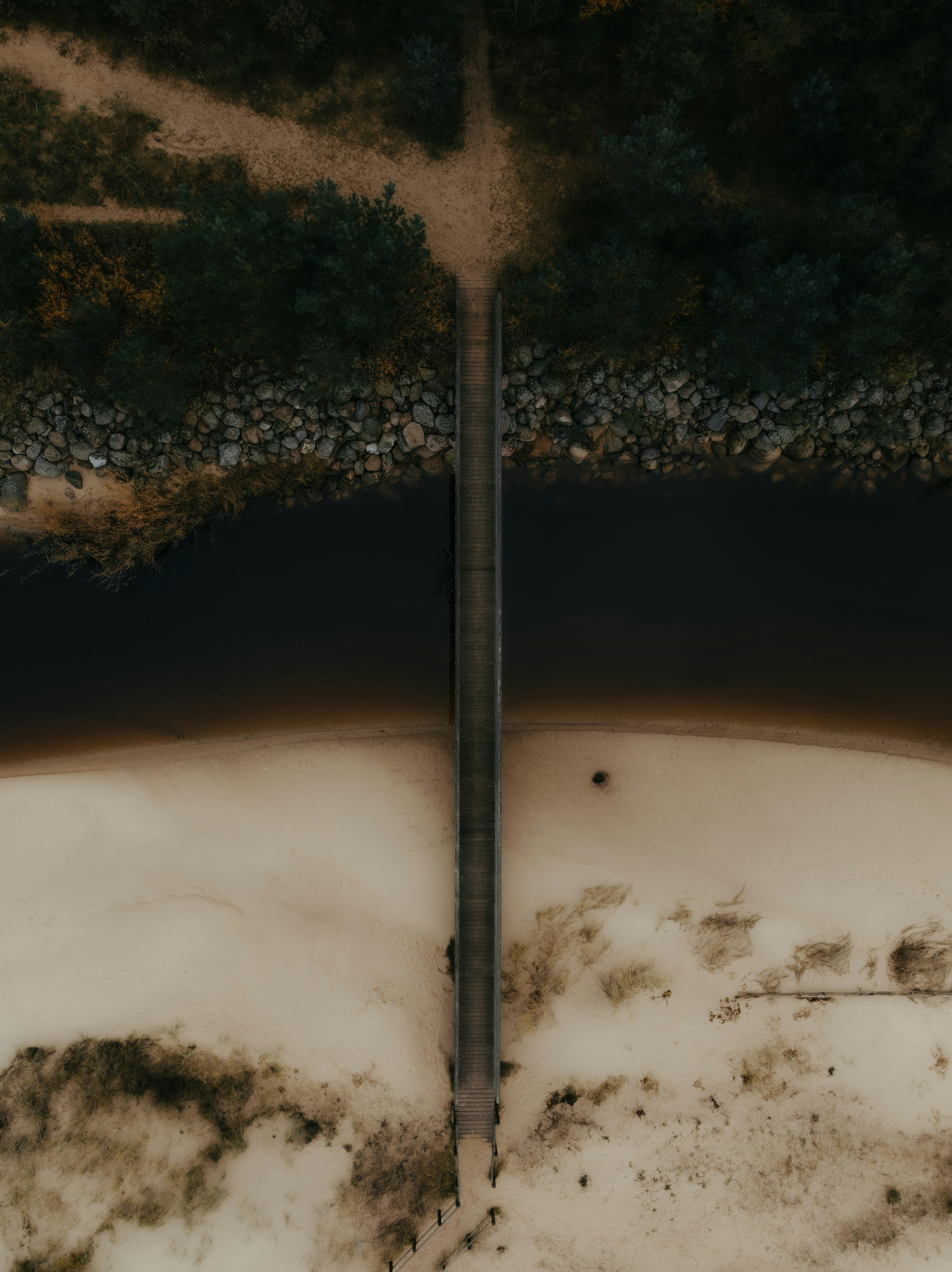 An Aerial View Of A Wooden Footbridge Crossing A Dark River To A Sandy Beach HD mobile wallpaper