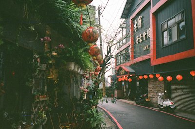 A Narrow Street In Jiufen With Red Lanterns Hanging Above And Potted Plants wallpaper preview