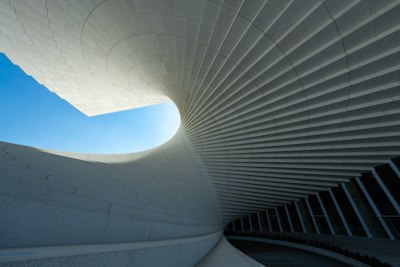 A Curved White Architectural Structure With Repeating Panels Against A Clear Blue Sky wallpaper preview