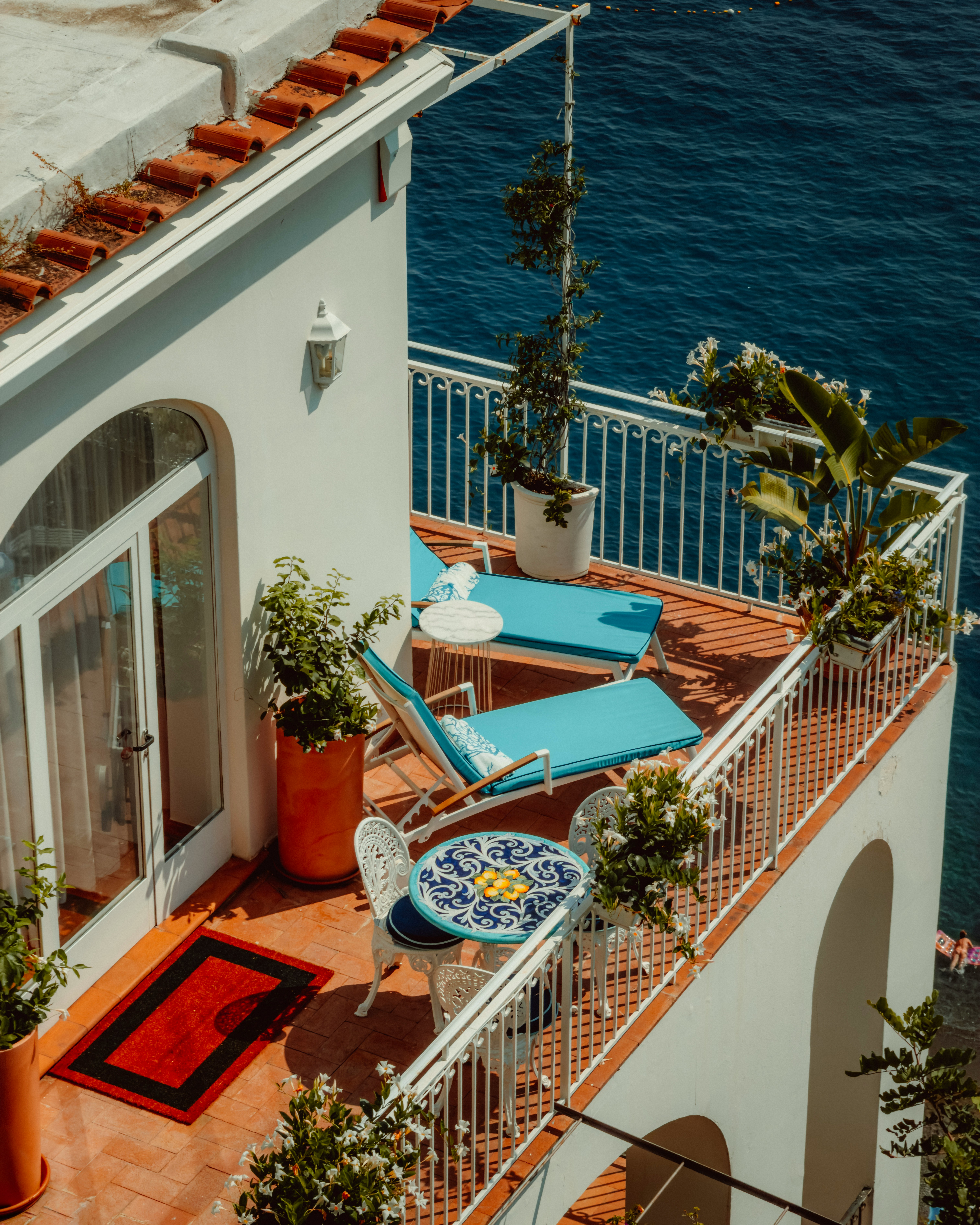 A Sunlit Balcony With Blue Lounge Chairs And A Tiled Table Overlooking The Sea HD mobile wallpaper