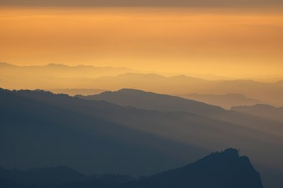 Layered Mountain Silhouettes Fading Into A Warm Orange Sky During The Golden Hour wallpaper preview