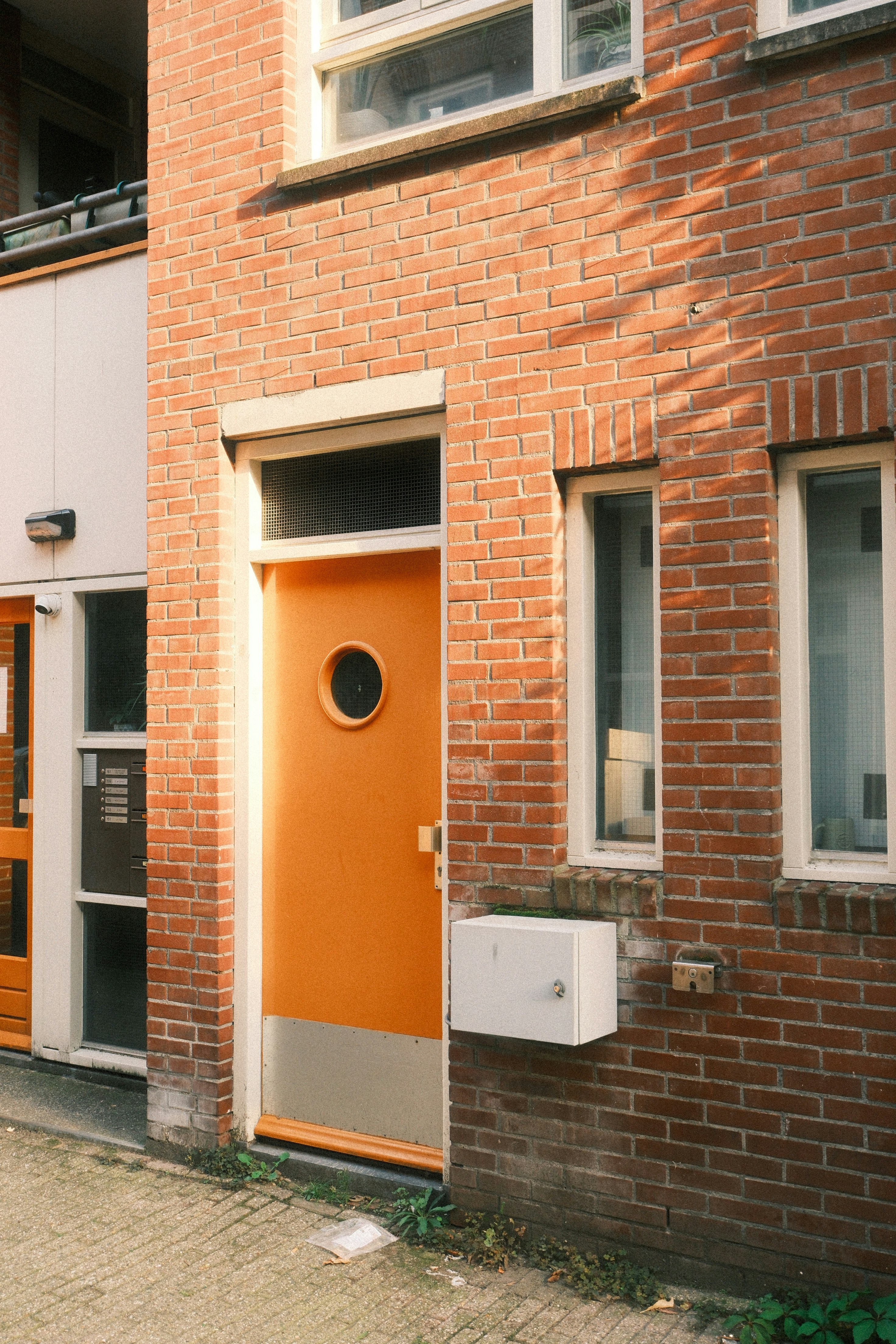 An Orange Door With A Circular Window In A Red Brick Building Facade HD mobile wallpaper